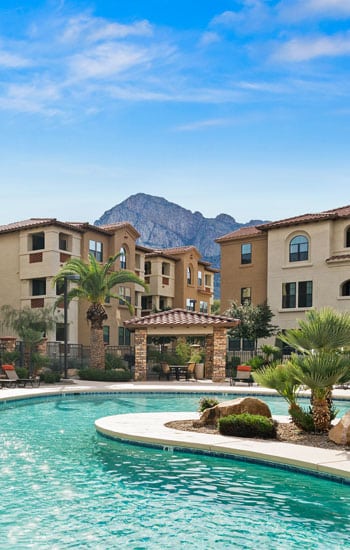 Tan and white adobe-style apartments overlook a tropical-style pool