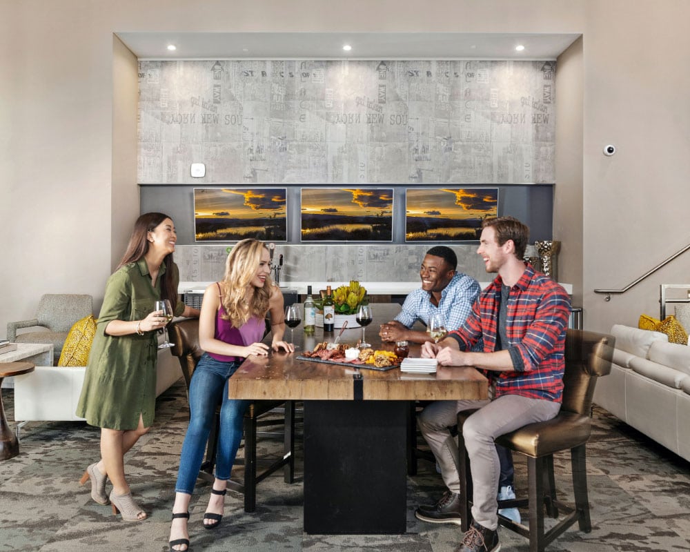 A group of friends laugh together around a table with a cheese tray