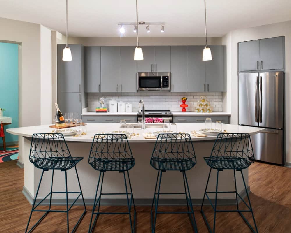 Interior kitchen rendering with gray cabinets, wireframe stools, and stainless steel appliances