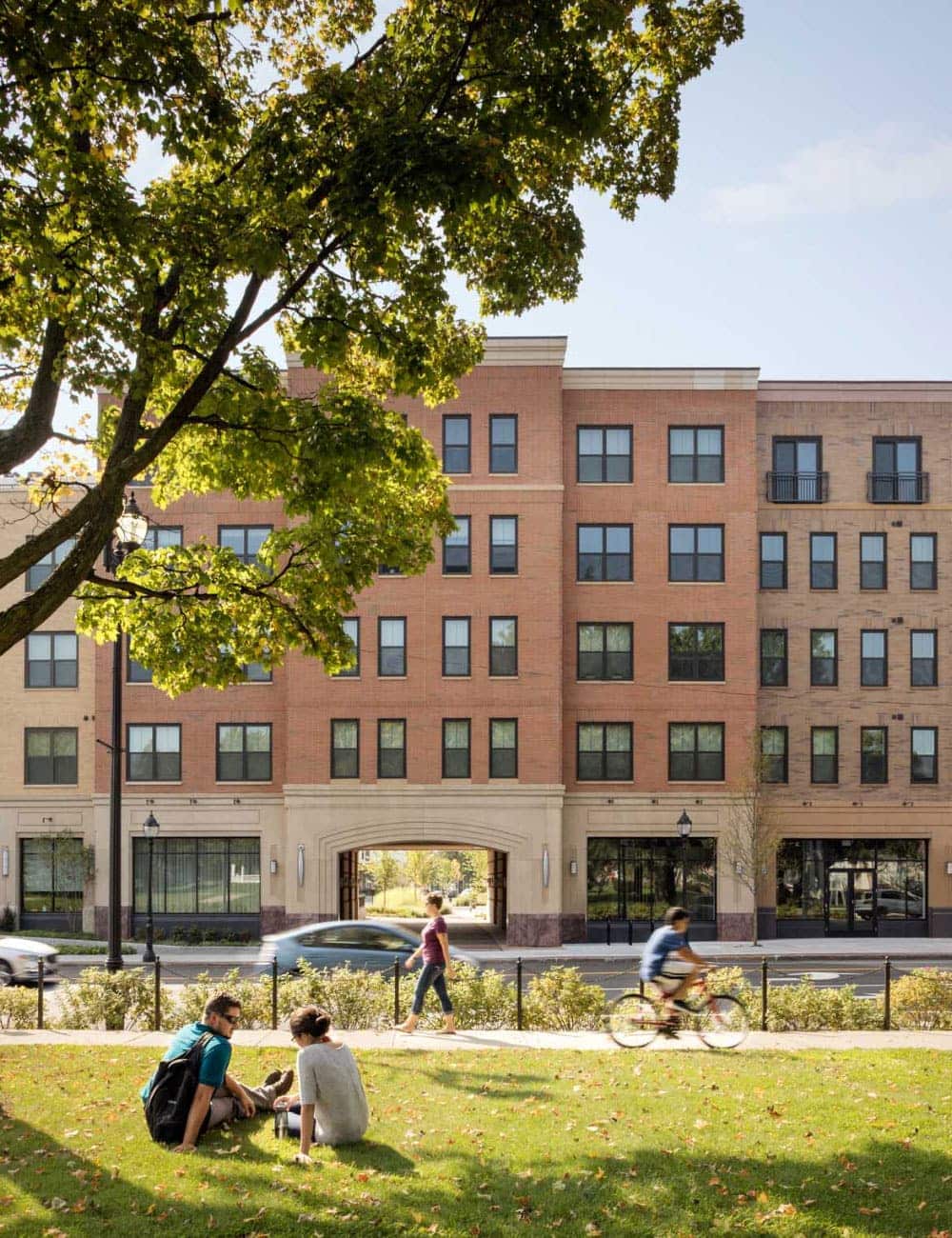 A couple sits in the grass across the street from The Merc apartments